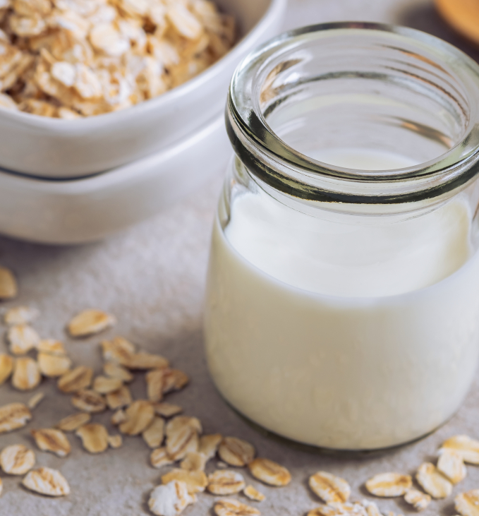 Bottle of oat milk and oat grains in bowl on table