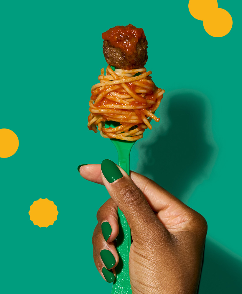 A hand holding a fork with spaghetti noodles and a meatball on the fork